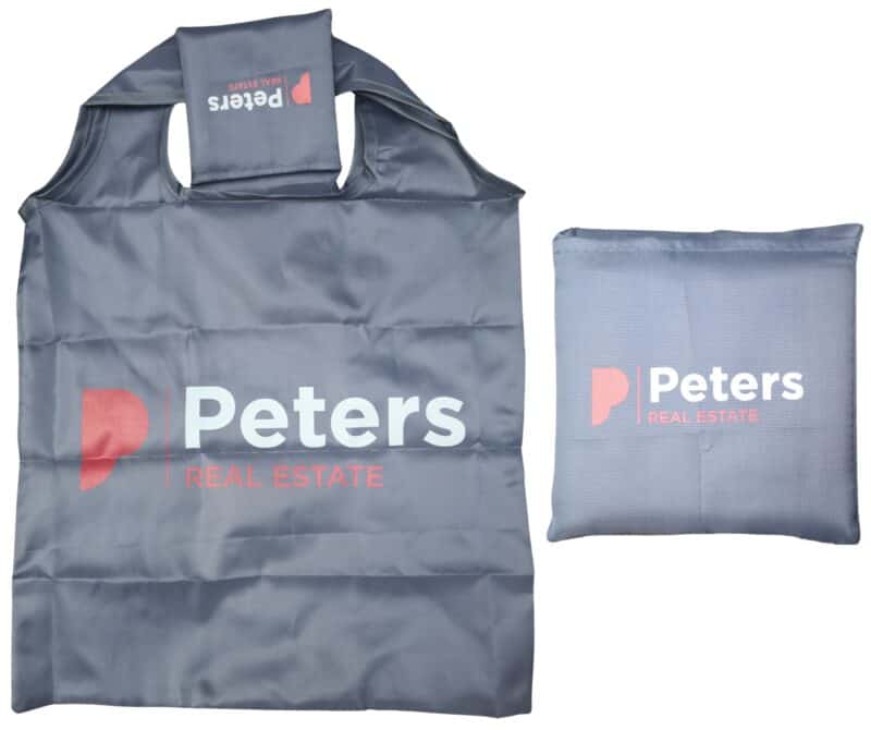 Promotional grey foldable shopping bag for Peters Real Estate, displayed unfolded and next to its folded pouch to show the logo."