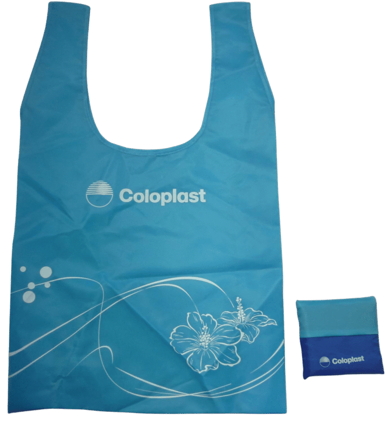 Light blue t-shirt style foldable shopping bag featuring the Coloplast logo and a white hibiscus flower design."