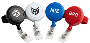 A collection of four custom retractable badge reels in different colours (black, white, blue, and red), each with a unique logo, showcasing the available variety.