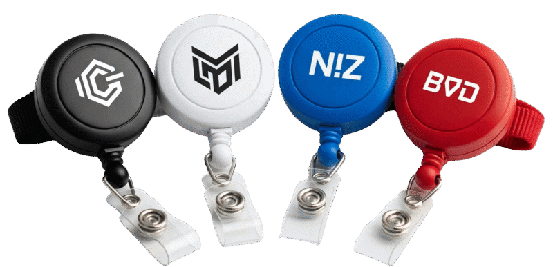 A collection of four custom retractable badge reels in different colours (black, white, blue, and red), each with a unique logo, showcasing the available variety.