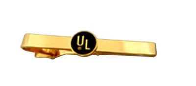 A gold plated custom tie bar with a circular logo with two letters printed on a black background.