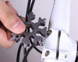 Picture of an 18 in 1 metal multi-tool being used by a person to tighten an allen key bolt on a bicycle.