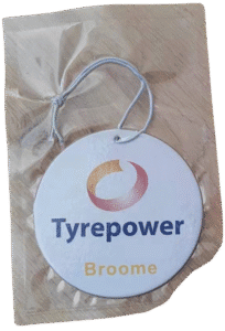 Packaged round custom car air freshener for 'Tyrepower Broome', featuring their orange and red swoosh logo with blue 'Tyrepower' text and yellow 'Broome' text on a white background. The air freshener is sealed in a clear wrapper with a light-colorued elastic hanging loop.