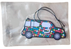 Packaged custom car air freshener shaped like a boxy van, branded with 'DRIVN' and a stylized 'D' logo. The van features a vibrant multi-coloured checkered square pattern and is shown sealed in a clear wrapper with a black elastic hanging loop.