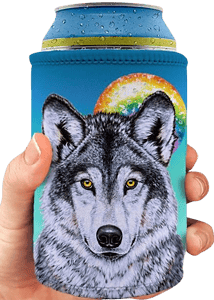A hand holds a light blue neoprene stubby holder encasing a silver beverage can with condensation droplets on its blue lid. The stubby holder features a detailed illustration of a grey and white wolf's head with piercing yellow eyes, facing forward. Behind the wolf is a circular rainbow design suggesting a moon or sun against a lighter blue background. This is a decorative can cooler with an animal and fantasy art theme.