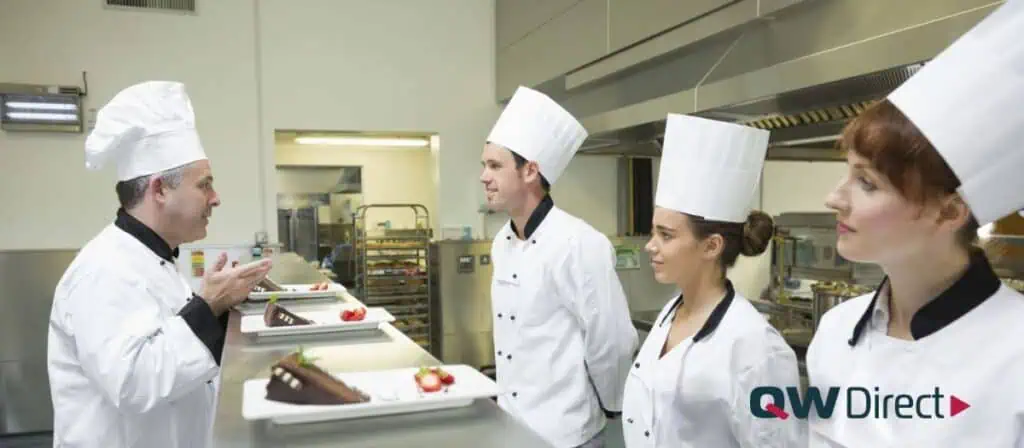  Confident chef smiling with arms crossed in a clean and organized commercial kitchen, symbolizing BOH efficiency and professionalism.