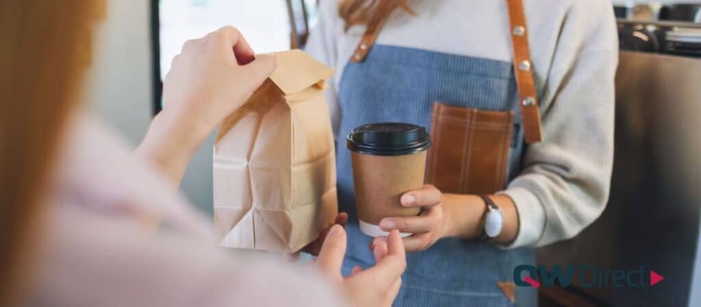  Cafe staff handing a paper takeaway cup to a customer, showcasing efficient service and eco-friendly packaging.