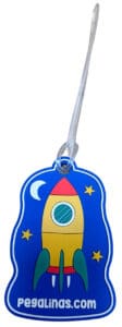 A custom rubber ID tag for 'pegalinas.com' in the shape of a rocket ship against a blue, starry background.
