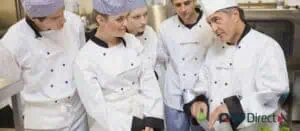 Chef demonstrating a technique to attentive kitchen staff, showcasing team training and operational consistency.