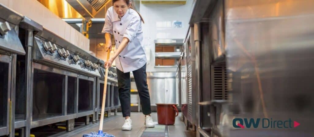 Staff member mopping the back-of-house kitchen floor using appropriate tools, highlighting efficient janitorial practices and hygiene compliance.