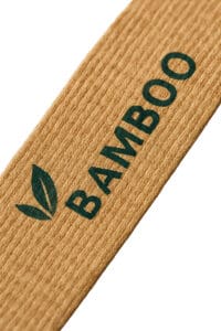 A close-up macro shot of a sustainable bamboo lanyard, showing the natural wood-like grain and a dark green printed logo.